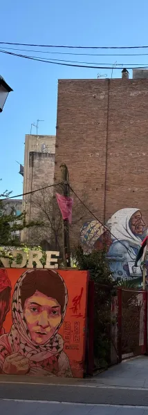 Mural młodej kobiety w chustce na pomarańczowej ścianie i murale starszych kobiet na ceglanym budynku w Barcelonie.