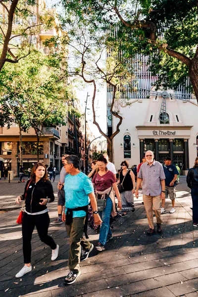 A group of diverse people walking on a sunny city street, passing El Molino theater in Barcelona.