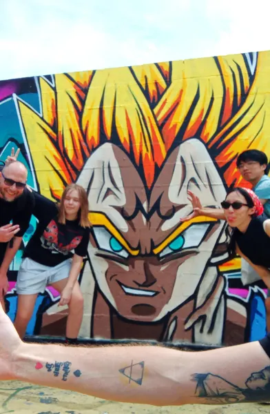 Group posing playfully with a Dragon Ball Z graffiti mural in Barcelona during a street art walking tour selfie.