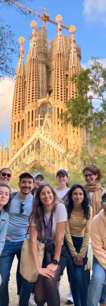 Un grupo diverso de personas sonriendo frente a la ornamentada, parcialmente construida basílica de la Sagrada Familia con...
