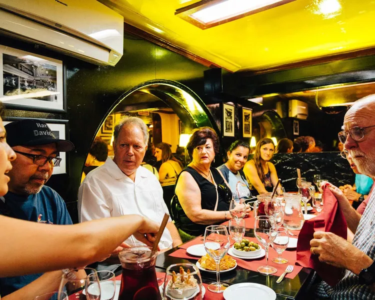 Eine Gruppe von Personen sitzt an einem Restauranttisch mit roten Tischdecken, teilt Tapas, Oliven und einen Krug Sangria.