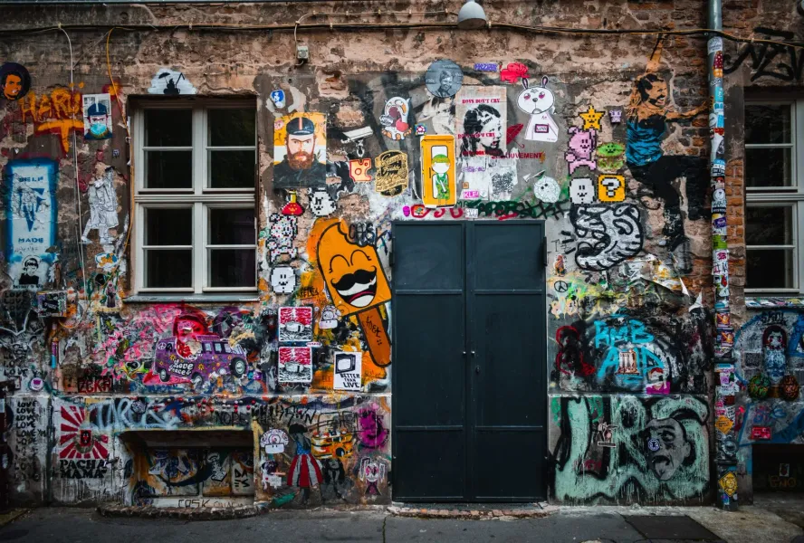 A weathered brick building facade in Berlin, densely covered with colorful street art, graffiti, and stickers.