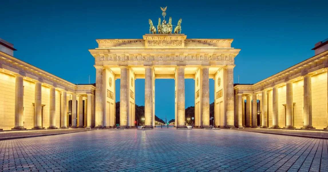 La Puerta de Brandenburgo en Berlín, iluminada al anochecer, con la escultura de la Cuadriga y una amplia plaza empedrada ...