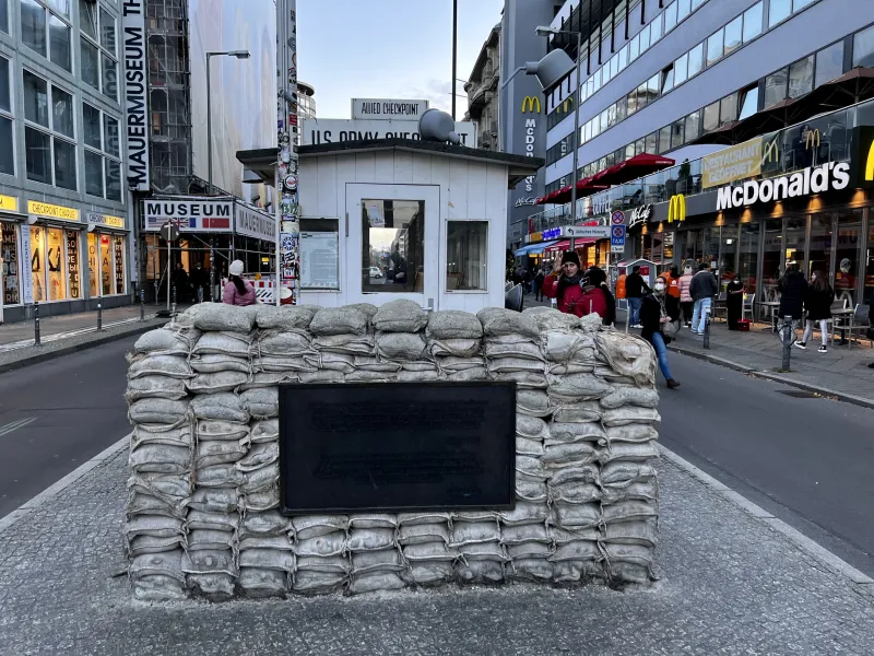 Reconstrucción de la caseta de guardia de Checkpoint Charlie con sacos de arena y placa en una calle adoquinada de Berlín.