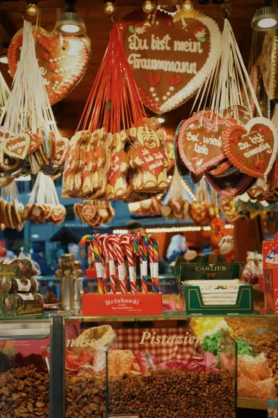 Ein Stand auf einem Weihnachtsmarkt, der Lebkuchenherzen, Zuckerstangen und geröstete Nüsse verkauft.