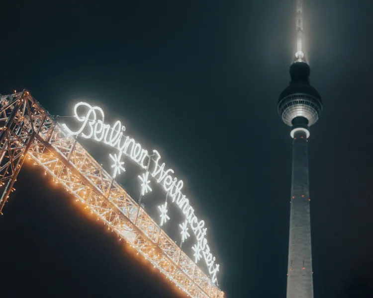 Beleuchtetes Schild 'Berliner Weihnachtszeit' und ein Teil des Berliner Fernsehturms vor dunklem Nachthimmel.