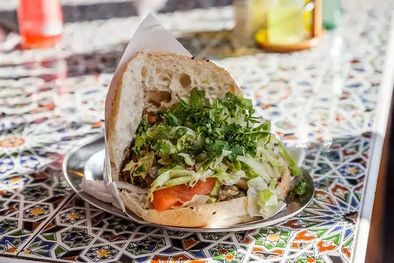 Halber Döner Kebab im Fladenbrot mit Fleisch, Salat, Petersilie und Tomate, auf einem Metallteller auf einem gekachelten T...