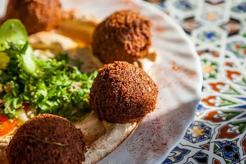 Nahaufnahme eines Tellers mit mehreren goldbraunen Falafelbällchen, Hummus und grünem Petersiliensalat.
