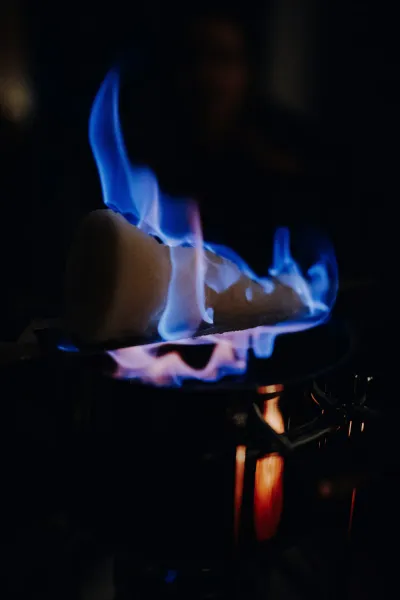 Zuckerhut mit blauen Flammen brennt über einem dunklen Topf, der den Vordergrund vor einem dunklen Hintergrund beleuchtet.