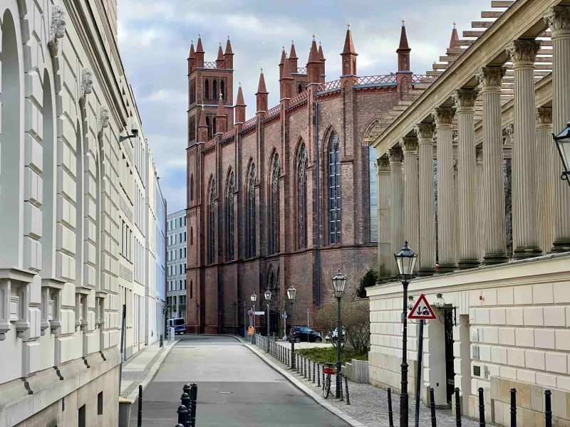 La iglesia Friedrichswerder de ladrillo rojo, vista desde una calle tranquila junto a un edificio con una columnata clásica.