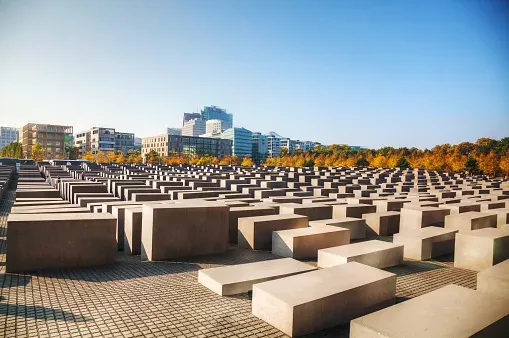 Estelas de hormigón del Monumento a los Judíos de Europa Asesinados en Berlín en un día soleado con edificios al fondo.