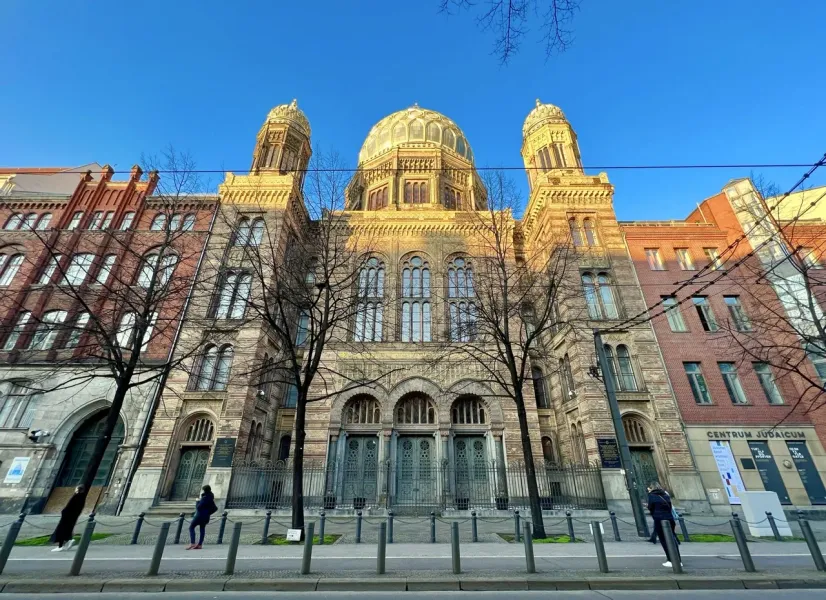 La fachada ornamentada de la Nueva Sinagoga de Berlín en un día soleado, vista desde el otro lado de la calle entre árboles.
