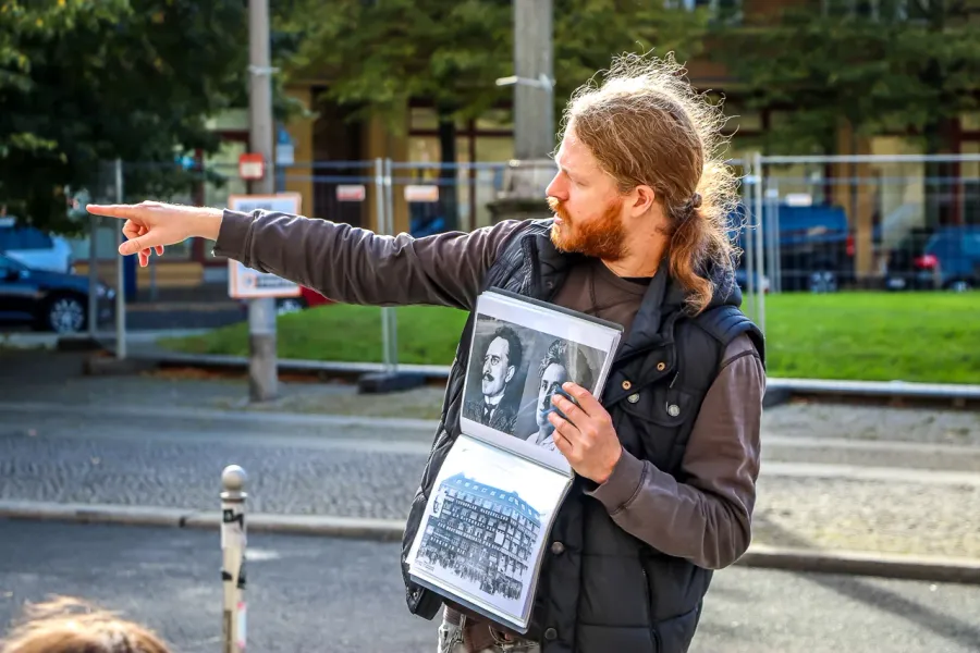 A tour guide in Berlin points while holding a binder with old black-and-white historical photographs.