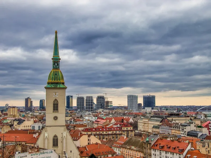St. Martin's Cathedral tower with green spire and clock face overlooking Bratislava's old town and modern city skyline under