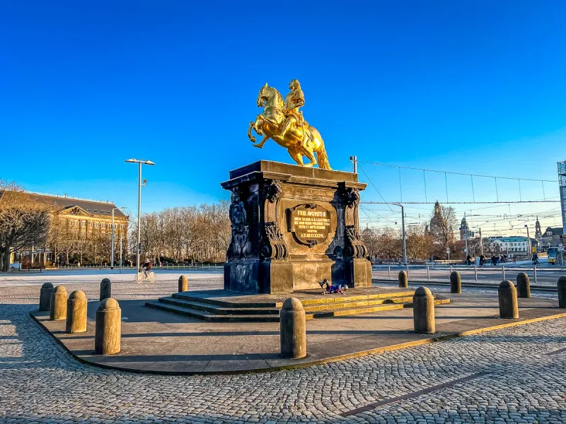 Goldene Reiterstatue Augusts des Starken auf dunklem Sockel auf einem Kopfsteinpflasterplatz in Dresden.