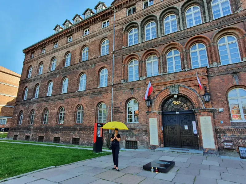 Historic brick building of the Polish Post Office in Gdansk with arched windows, a dark entrance, and Polish flags. A pers...