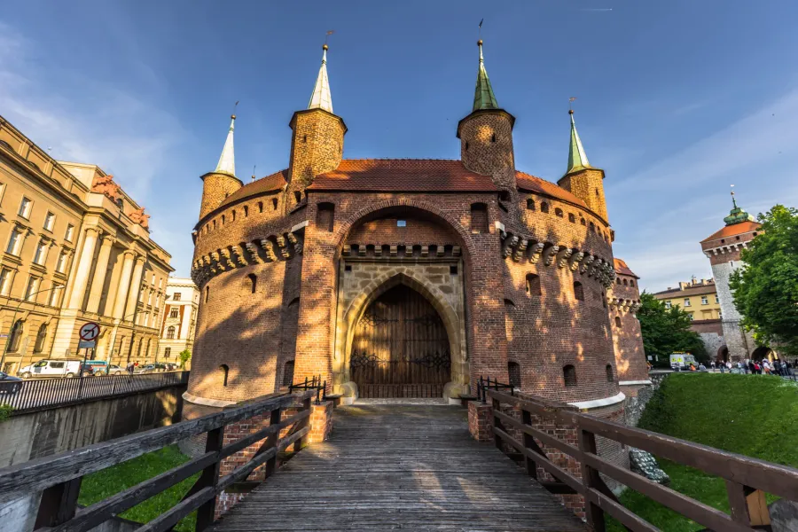 Krakowski Barbakan, okrągła forteca z czerwonej cegły, widziany z drewnianego mostu wejściowego w słoneczny dzień.