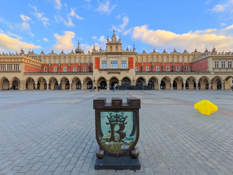 La Lonja de los Paños en la Plaza del Mercado de Cracovia al atardecer, con una caja de donativos y un paraguas amarillo.