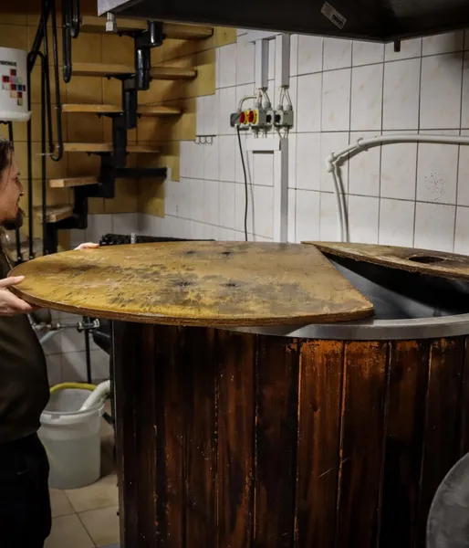 Ein Brauer öffnet den Holzdeckel eines großen Gärbottichs in einer kleinen Brauerei.