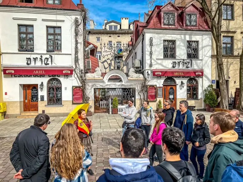 Un grupo de turistas escucha a una guía con un paraguas amarillo en la calle Szeroka del barrio de Kazimierz, Cracovia.