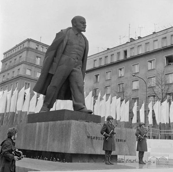Schwarz-Weiß-Archivfoto der großen Lenin-Statue in Nowa Huta, mit zwei Soldaten, die an ihrem Sockel Wache stehen.