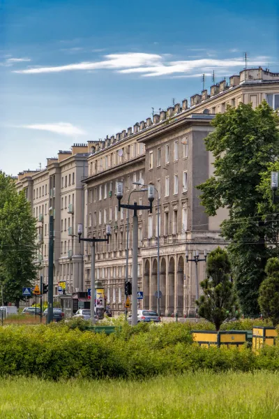 A wide street in Nowa Huta, Krakow, with long socialist realist apartment blocks, green trees, and a blue sky.