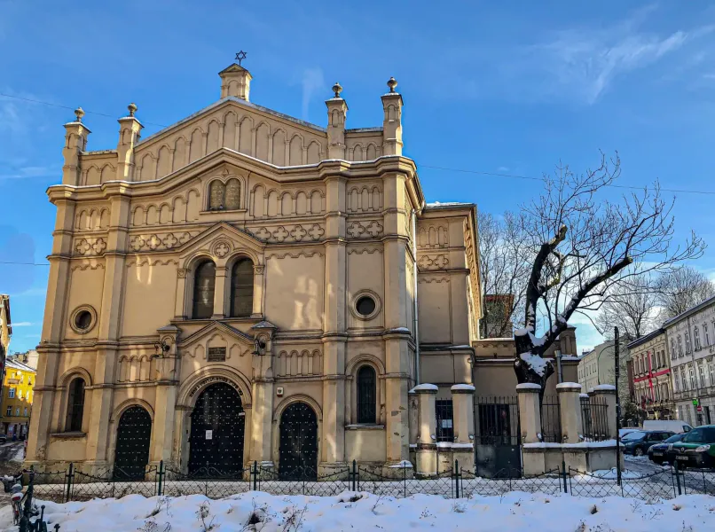 Exterior view of a large, ornate synagogue with a Star of David, covered in snow, under a clear blue sky in Krakow.