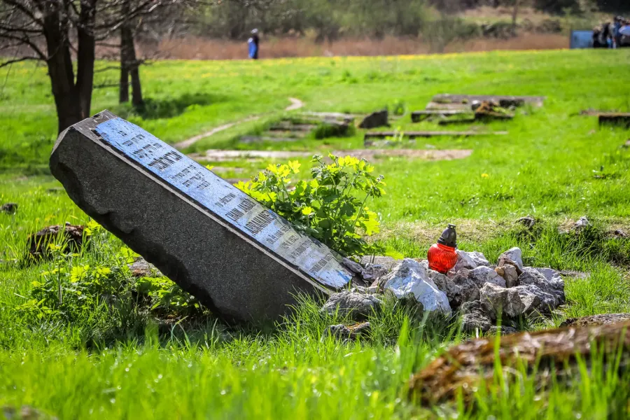 Ein geneigter Grabstein mit einer blauen Tafel und einer roten Grabkerze auf einem grasbewachsenen Feld der Gedenkstätte P...