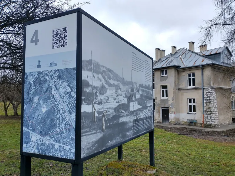 Eine Informationstafel mit Karte und historischen Fotos steht auf einer Wiese vor dem „Grauen Haus“ auf dem Lagergelände P...