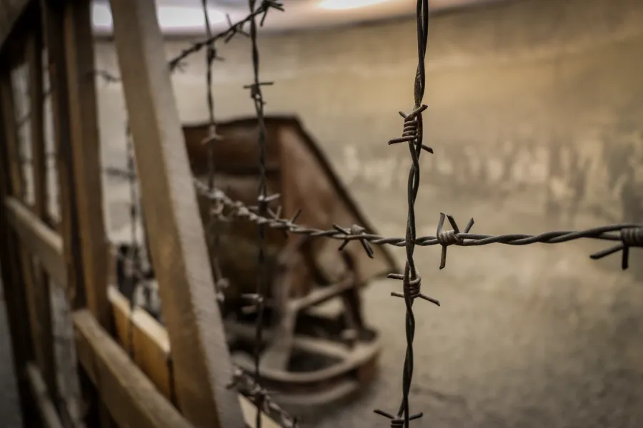 Close-up of barbed wire in an exhibit at Schindler's Factory Museum, with a blurred wheelbarrow in the background.