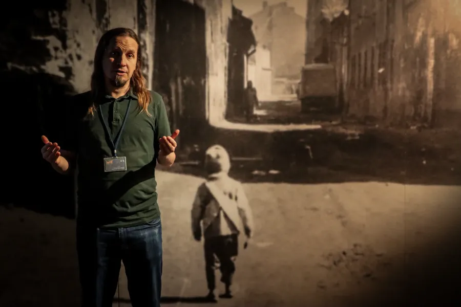 A tour guide gestures while speaking in front of a large historical photograph inside a museum exhibit.