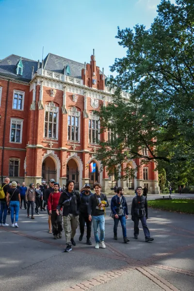 Eine Reisegruppe geht an einem sonnigen Tag an der neugotischen Backsteinfassade des Collegium Novum in Krakau vorbei.