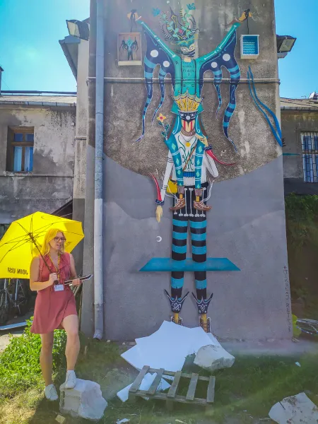 Una guía turística con un paraguas amarillo de pie frente a un gran mural colorido en un edificio de Cracovia.