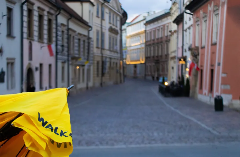 Ein gelber Walkative-Führungsschirm im Vordergrund, mit unscharfem Blick auf eine Gasse in der Krakauer Altstadt.