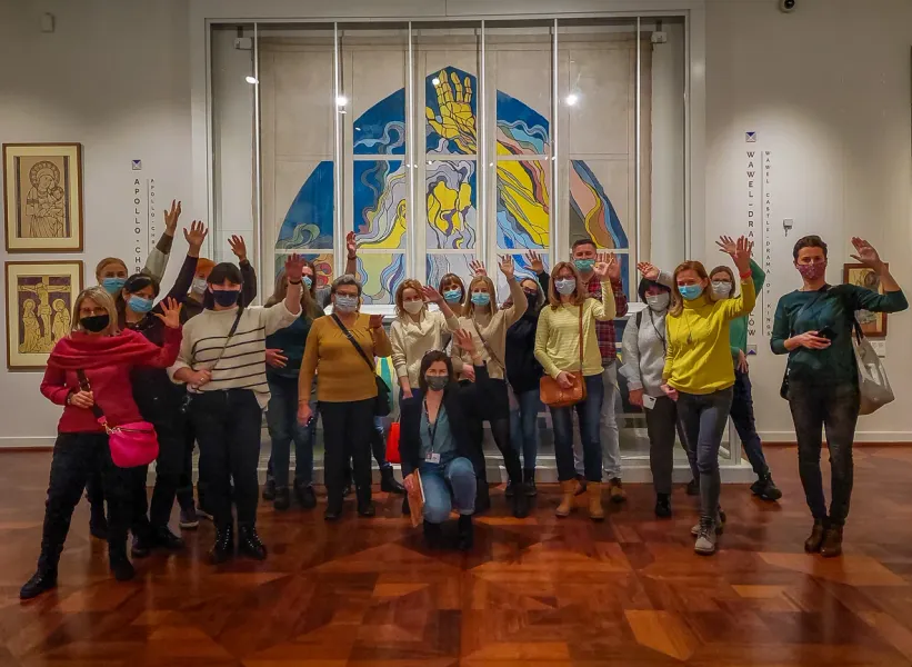 Eine Gruppe von Touristen mit Gesichtsmasken winkt in einem Museum vor einem großen, modernen Kunstwerk.