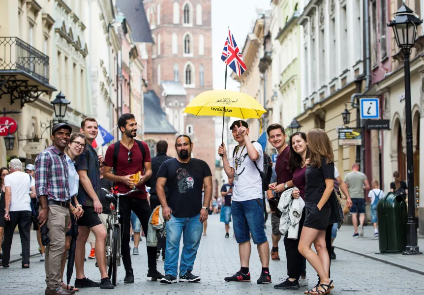 Un grupo de turistas con un guía que sostiene un paraguas amarillo en una calle adoquinada del casco antiguo de Cracovia.