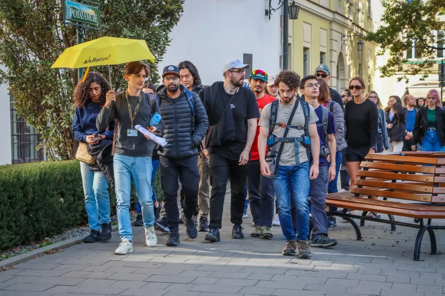 Un guía de Walkative con un paraguas amarillo lidera a un grupo diverso de turistas por una acera de Cracovia.
