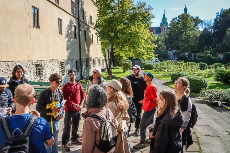 Eine Gruppe von Touristen hört einem Führer auf dem Wawelhügel in Krakau zu, im Hintergrund sind die Domtürme zu sehen.
