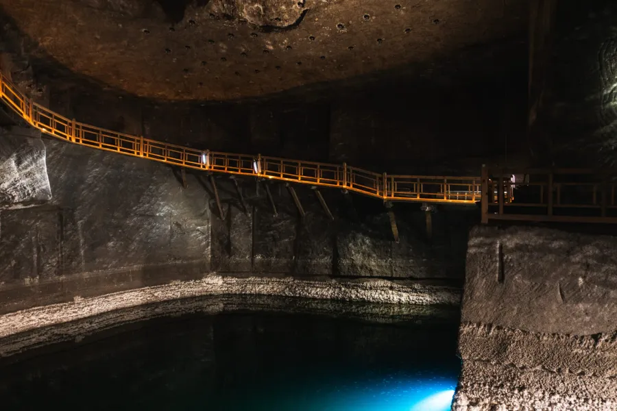 An illuminated wooden walkway runs along the cavern wall above an underground brine lake in the Wieliczka Salt Mine.