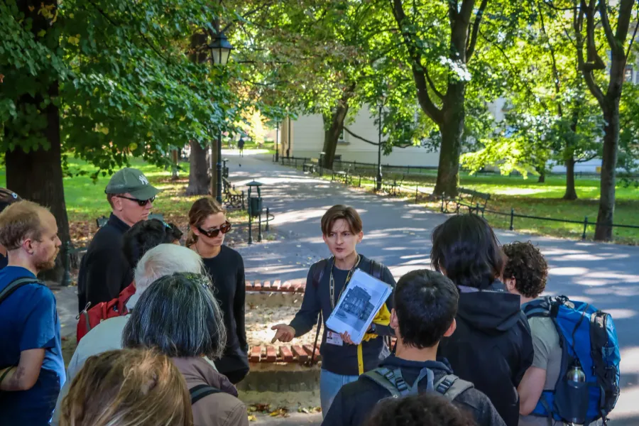 Eine Reiseführerin zeigt einer Gruppe von Personen auf einem Weg in einem sonnigen Park in Krakau historische Fotos.