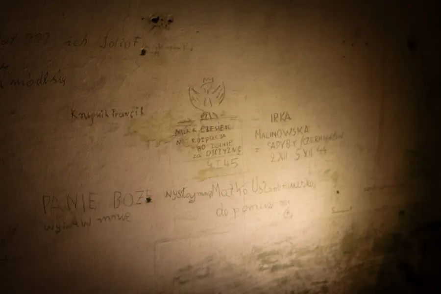 Pared tenuemente iluminada con inscripciones en polaco de la Segunda Guerra Mundial y el dibujo de un águila polaca.