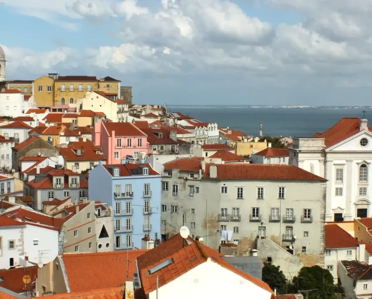Blick auf das Alfama-Viertel in Lissabon mit roten Dächern, dem Nationalen Pantheon und dem Fluss Tejo.