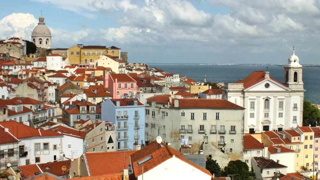 Vista del barrio de Alfama en Lisboa con tejados rojos, el Panteón Nacional y el río Tajo al fondo.