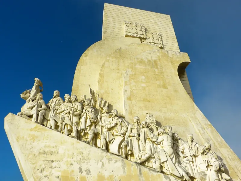Stone Monument to the Discoveries in Lisbon featuring statues of historical explorers on a ship's prow against a blue sky.