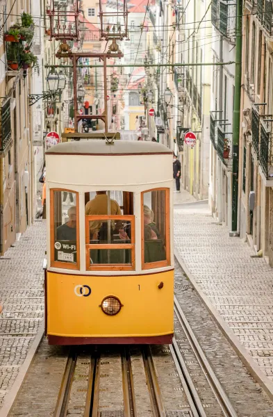 Yellow funicular tram climbing a steep cobbled street lined with historic buildings in Lisbon.