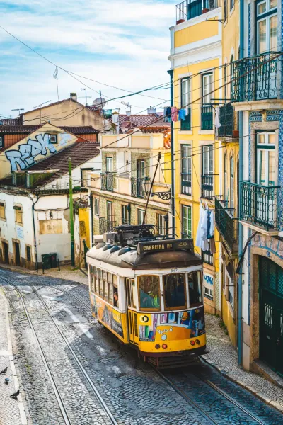 Yellow Tram 28 climbing a steep, cobbled street lined with traditional tiled buildings in Lisbon.