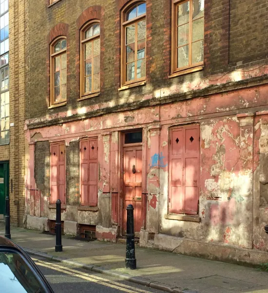 A 1700s weathered brick building with a faded pink ground-floor storefront, viewed from a street in London.