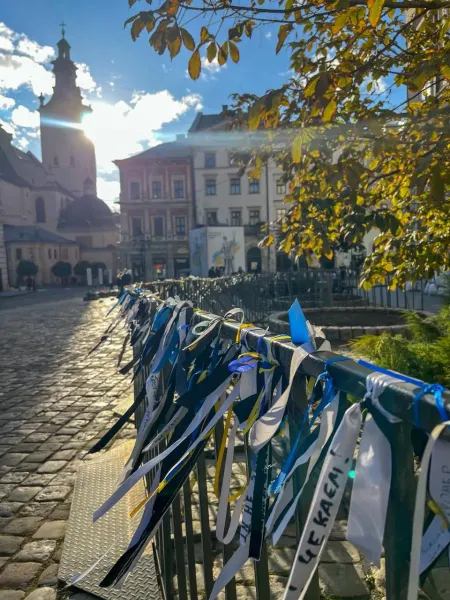 A fence along a cobblestone street in Lviv, adorned with many blue and yellow ribbons. St. Andrew's Church and historic bu...