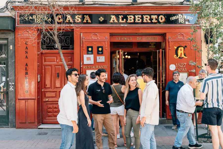 Un guía turístico habla con los turistas frente a la fachada roja de la histórica taberna Casa Alberto de Madrid.
