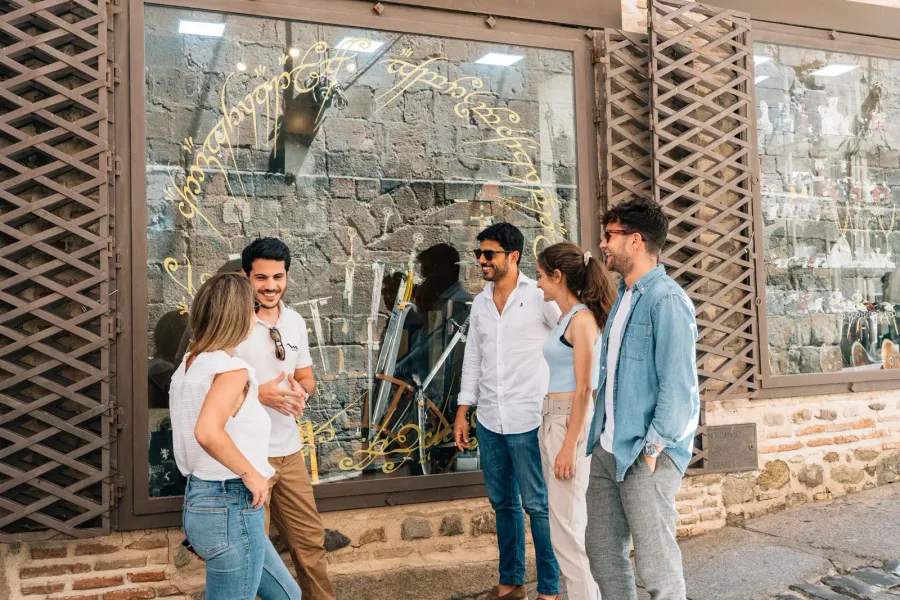 Un grupo de cinco jóvenes conversando frente a una tienda con una inscripción dorada en el escaparate.